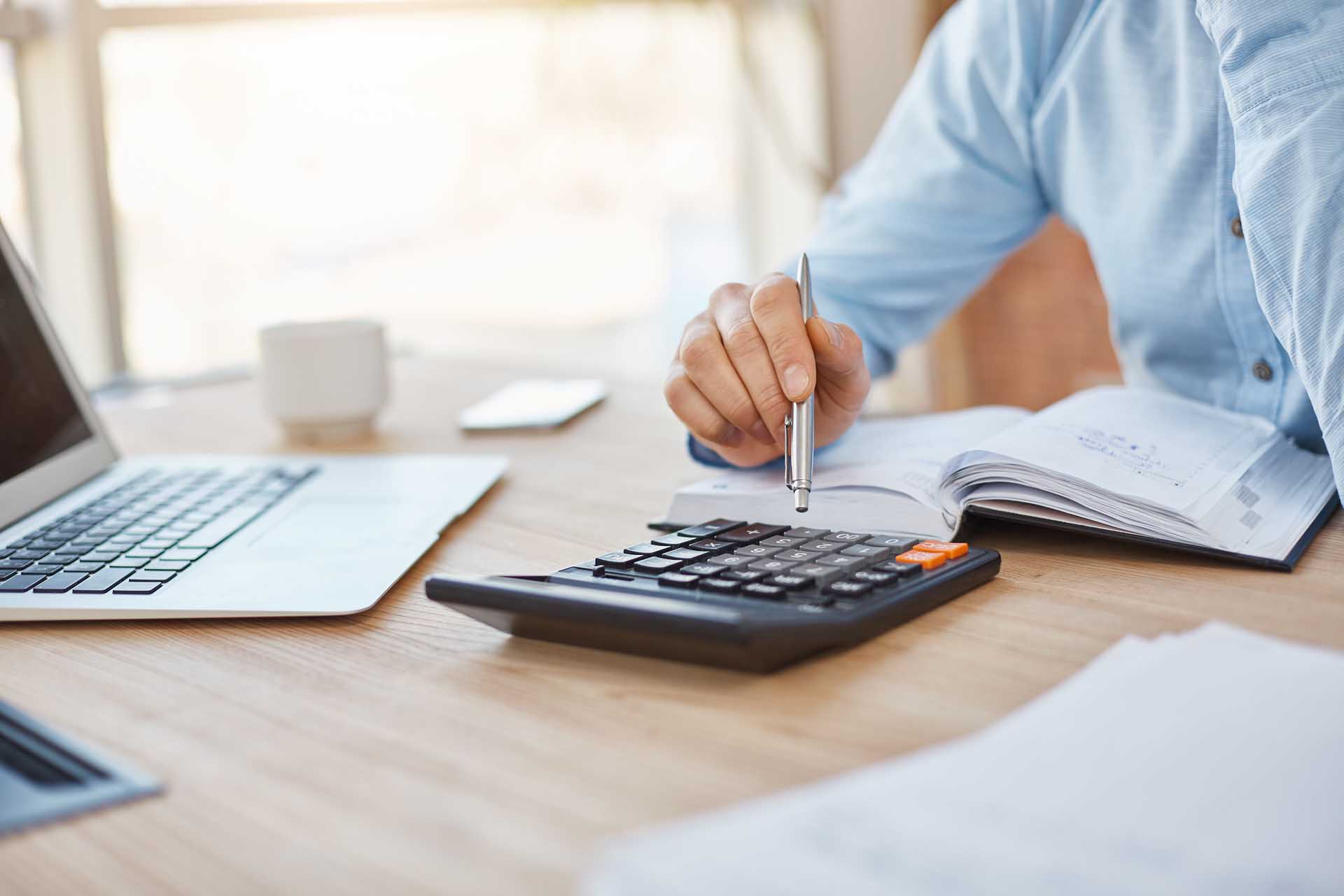 Close up detail of professional serious accountant sitting in light office, checking company finance profits on calculator, writing down results in notebook. Business concept.